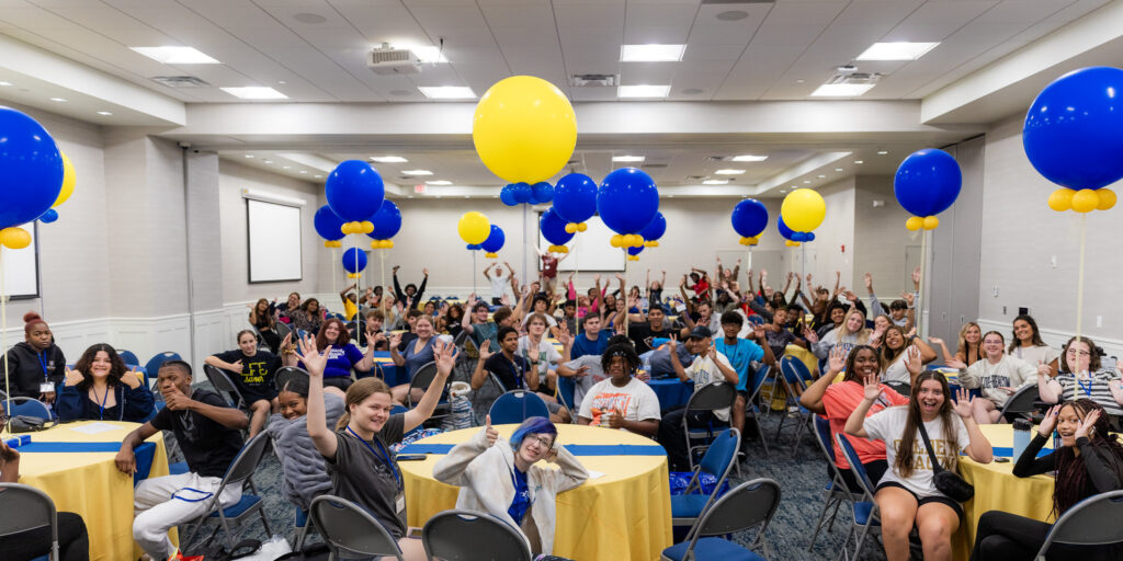 Students cheer underneath bright yellow and blue balloons during Goldey-Beacom College's new student orientation.