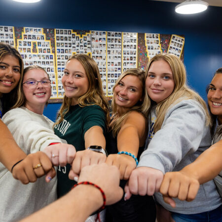 New students enjoying orientation at Goldey-Beacom College with a group fist bump in front of a photo collage spelling out 